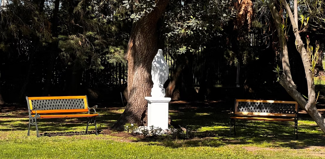 Imagen de la Virgen entre los bancos del parque